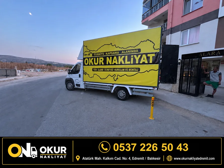 Okur Nakliyat aracı bir apartmanın önüne yanaşmış, kasasındaki sarı brandada marka adı okunuyor