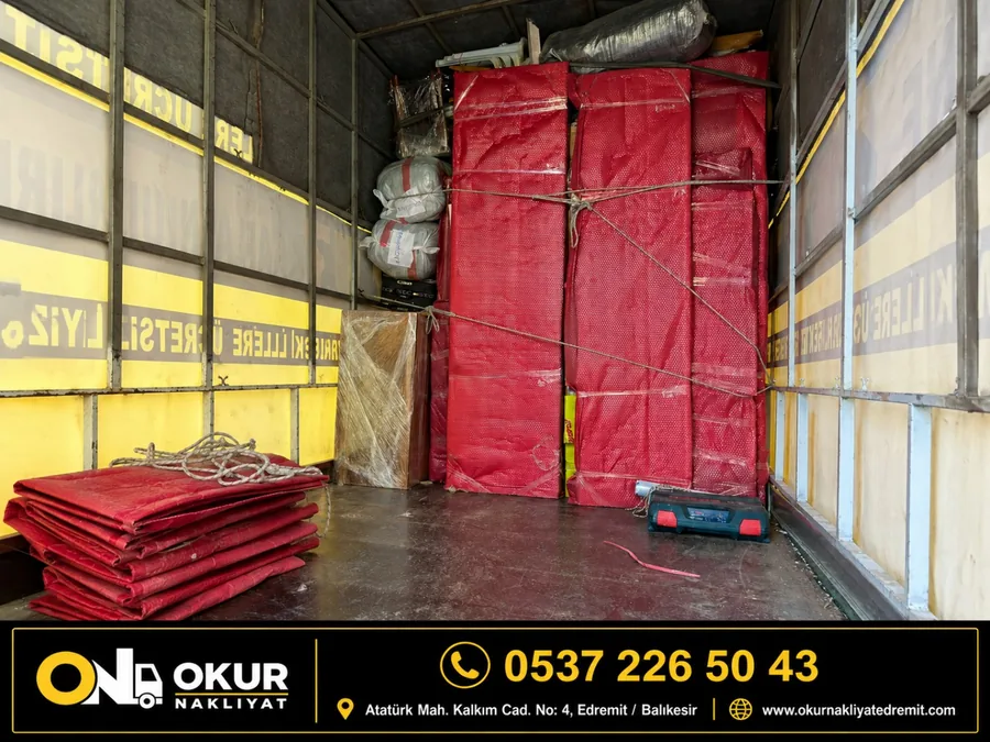 Okur Nakliyat aracının içinde kırmızı koruyucu battaniyelere sarılmış ve halatlarla sabitlenmiş mobilyalar